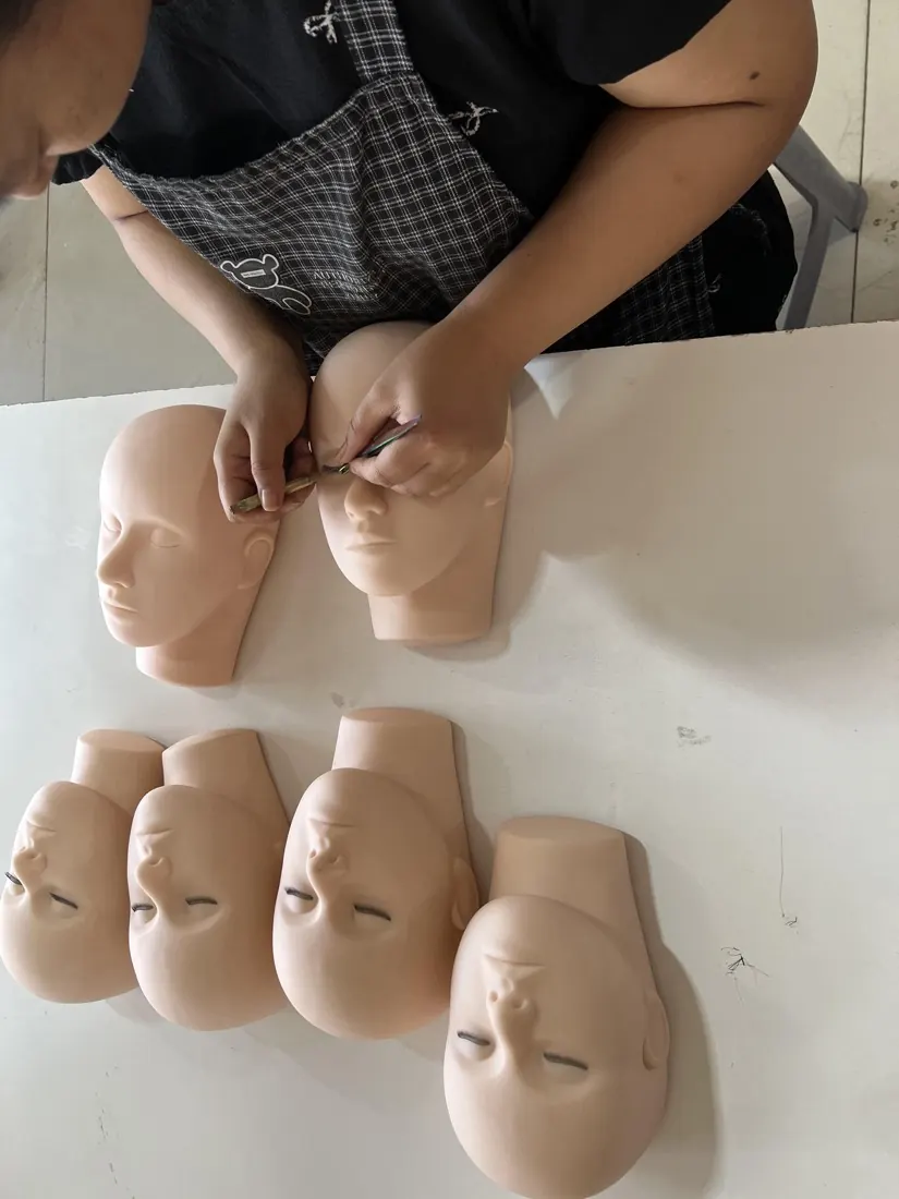 Hand-implanting lashes into a mannequin head with tweezers